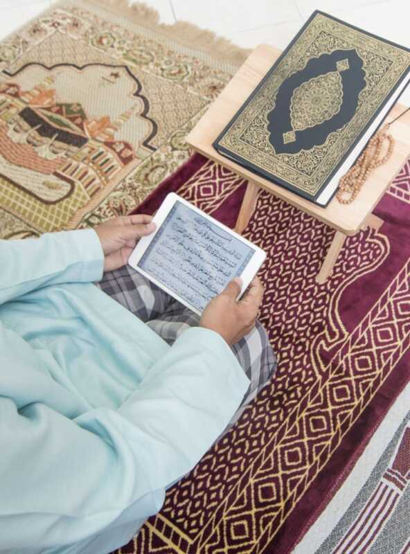 Asian Muslim man reading digital Al-Quran using tablet at home during Ramadan