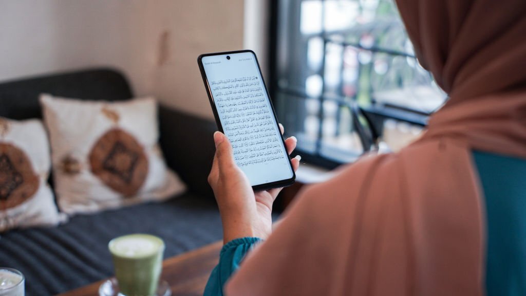 Hijab Woman Reading Quran on Smartphone Apps over the soulder